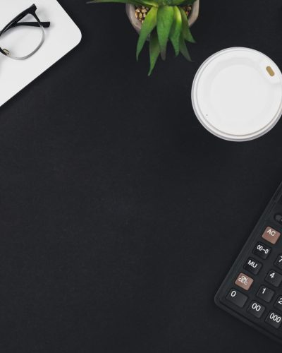 Laptop, coffee cup, notepad and calculator on black background, top view, workplace, copy space.